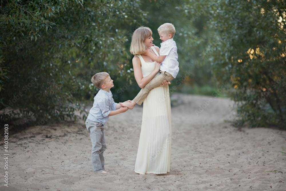 mother in a long dress holding her son's blond, and older brother tickle him heel