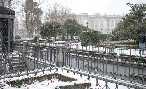a figures of a different green plants and trees covered by the snow in front of a big ancient building in a cold winter snowfall day