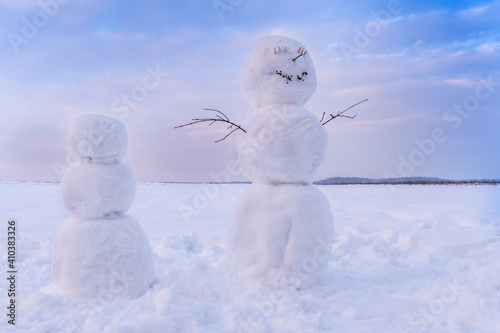 Beautiful, happy snowman standing on the background of a blue sky with clouds and another snowman not completely made. Beautiful winter background with snowmen.