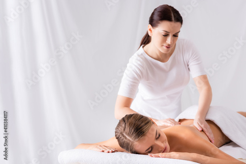 Brunette masseur massaging back of woman on massage table in spa salon