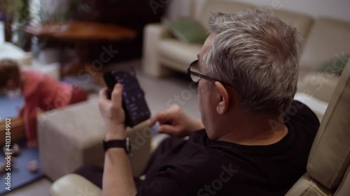 Man browisng phone in living room with child playing on floor. Shallow depth of field. Over the shoulder view. photo