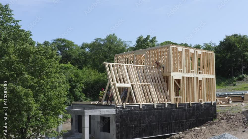 Aerial view of exterior of unfinshed frame house, workers carefully are lifting up the wall on the second floor. Aerial view of exterior of unfinshed frame house, workers carefully are lifting up the wall on the second floor.