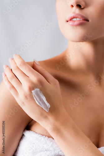 cropped view of young woman with bare shoulder and cream on hand on white