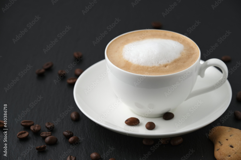 Cookies and coffee. White cup with cappuccino on a black table, white background. Coffee beans on the table. Cookies and coffee. White cup with cappuccino on a black table, white background. Coffee beans on the table.