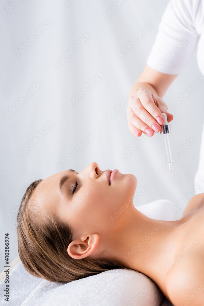 beautician holding pipette with serum near woman in spa salon