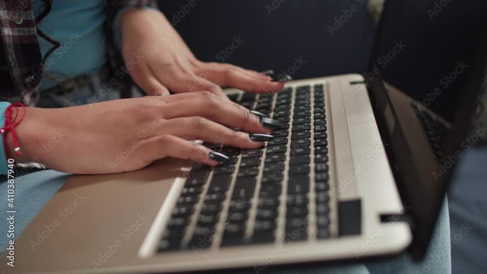 Black female hands with perfect manicured nails typing on laptop keyboard while networking online indoors.