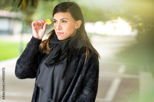 Ragazza mora vestita di nero tiene una foglia gialla autunnale in mano in un parco photo