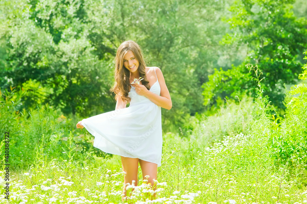 Smiling young woman in white dress with flower against background of summer green park. Beautiful healthy happy girl enjoying freedom outside in nature. Smiling young woman in white dress with flower against background of summer green park. Beautiful healthy happy girl enjoying freedom outside in nature.