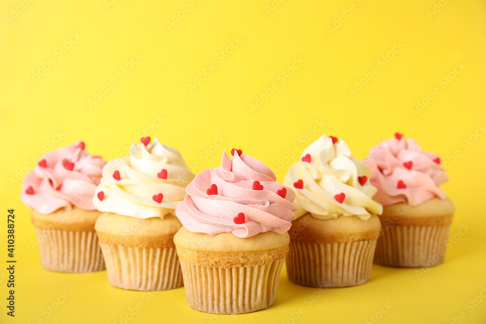 Tasty cupcakes with heart shaped sprinkles on yellow background. Valentine's Day celebration