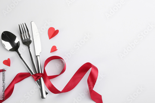 Cutlery set and red ribbon on white background, flat lay with space for text. Valentine's Day dinner