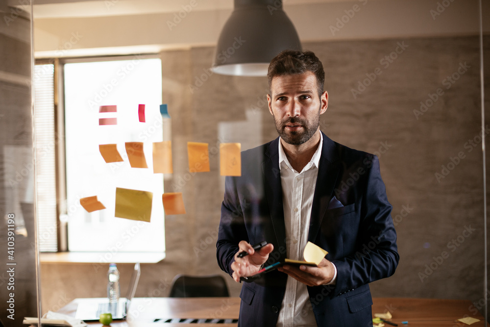 Fototapeta premium Businessman in conference room use sticky notes on glass wall. Handsome businessman making a business plan..