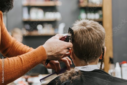 the process of cutting a blond boy with a long braid in a chair in a barbershop salon, a barbershop concept for men and boys