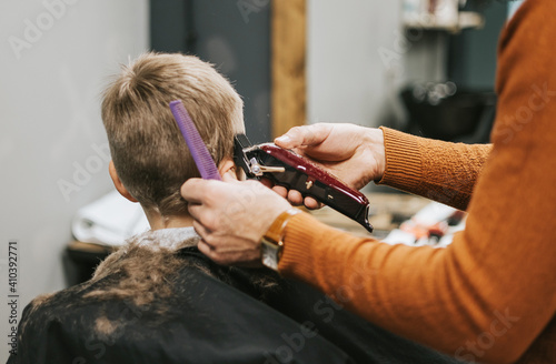 the process of cutting a blond boy with a long braid in a chair in a barbershop salon  a barbershop concept for men and boys