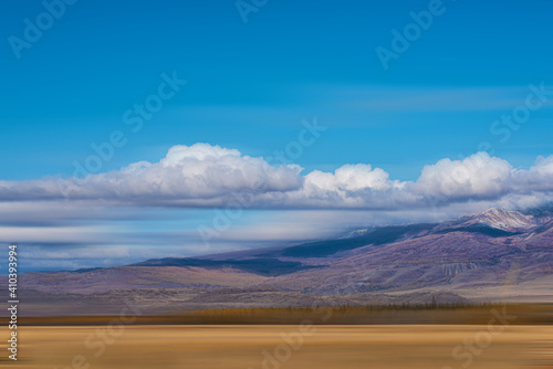 panoramic view of plain at root of snow-covered mountains on blue sky background