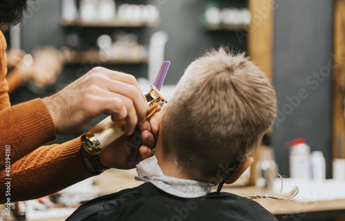 the process of cutting a blond boy with a long braid in a chair in a barbershop salon, a barbershop concept for men and boys