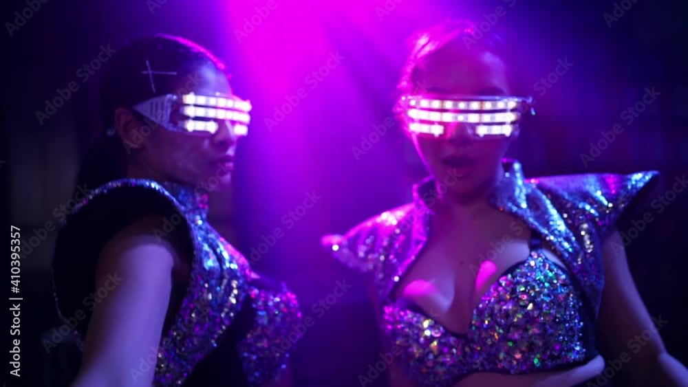 Two confidence woman friend wear LED glowing glasses dancing in night club with multi-color illuminated neon night lights at night club. Group of female enjoy and having fun nightlife dance party. Two confidence woman friend wear LED glowing glasses dancing in night club with multi-color illuminated neon night lights at night club. Group of female enjoy and having fun nightlife dance party.