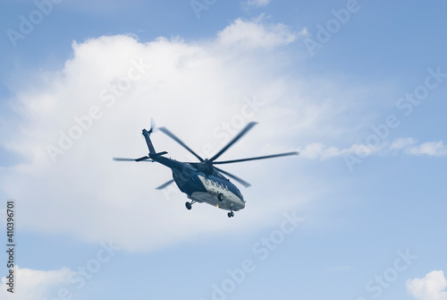 High in the sky with beautiful clouds, a passenger helicopter is flying, painted in blue and gray. Close-up