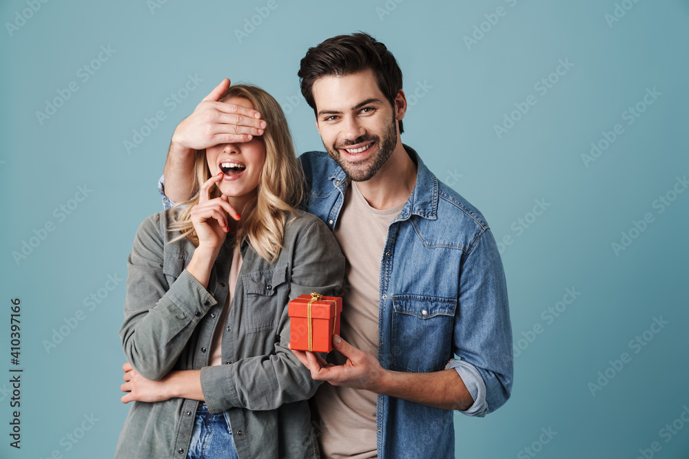 Young happy man with gift box covering eyes of excited girl Young happy man with gift box covering eyes of excited girl