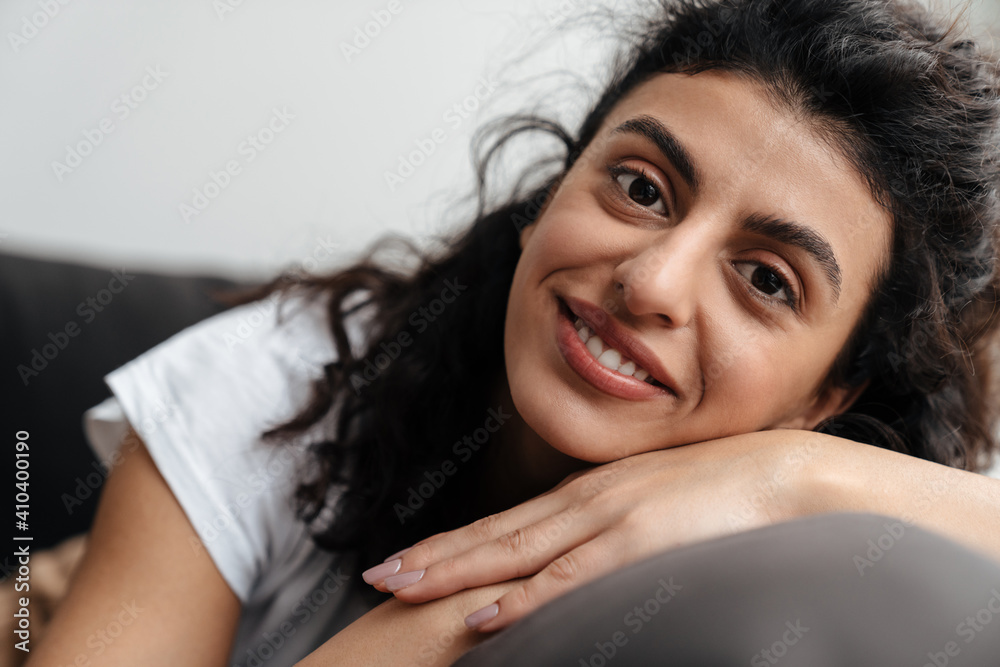 Happy brunette young woman smiling at camera while resting on sofa Happy brunette young woman smiling at camera while resting on sofa