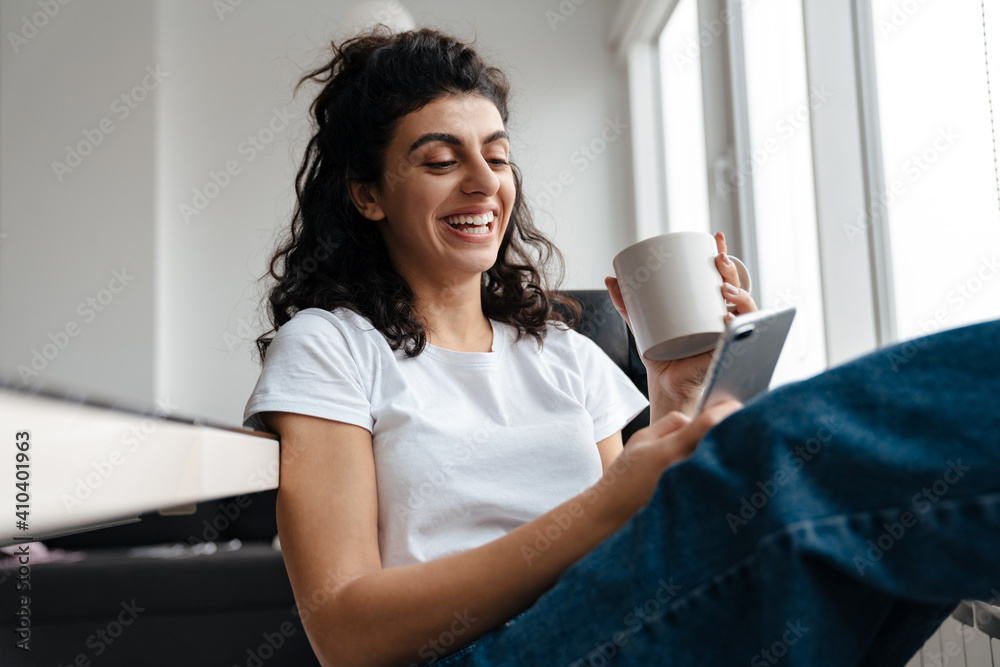 Laughing brunette woman using mobile phone while drinking coffee Laughing brunette woman using mobile phone while drinking coffee