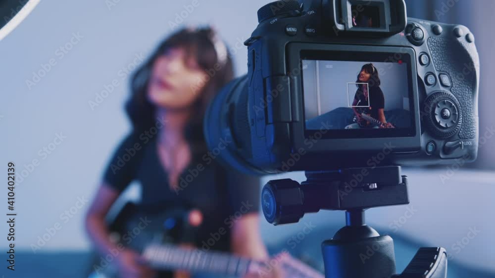Young woman playing guitar in front of the camera. recording demo or giving online class. High quality 4k footage