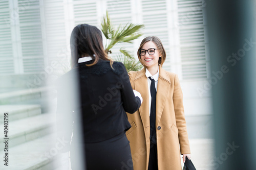 colleghe manager si incontrano in contesto business in esterni vicino ad un palazzo moderno fatto di specchi: Parlano entrambe al telefono mentre camminano photo