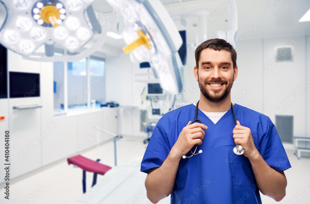healthcare, surgery and medicine concept - happy smiling doctor or male nurse in blue uniform with stethoscope over operating room at hospital on background