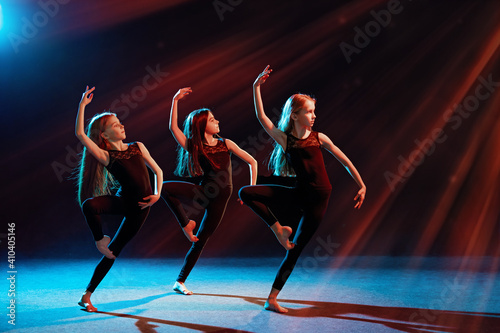 group of three ballet girls in tight-fitting costumes dance against black background with their long hair down  silhouettes illuminated by color sources.