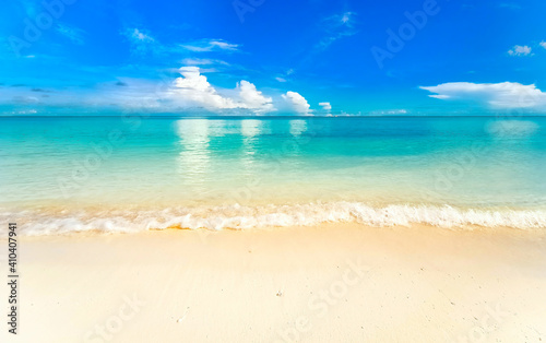 Beautiful background image of tropical beach. Light surf wave with white foam. Blue summer sky  white clouds reflected in turquoise clear water ocean. Relaxation and rest.