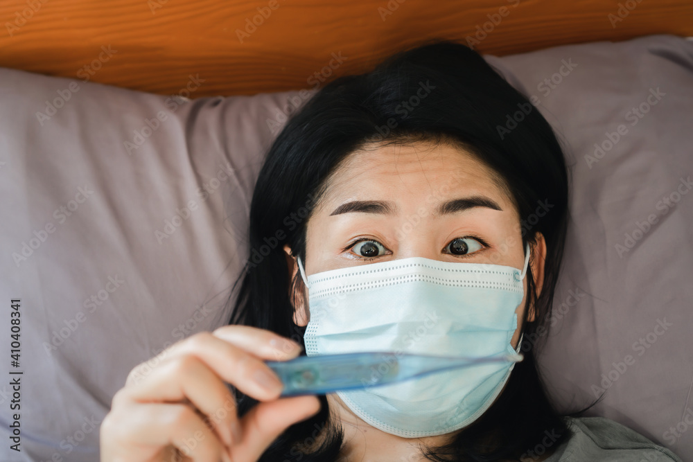 shocked Asian woman checking her high temperature by thermometer in bed