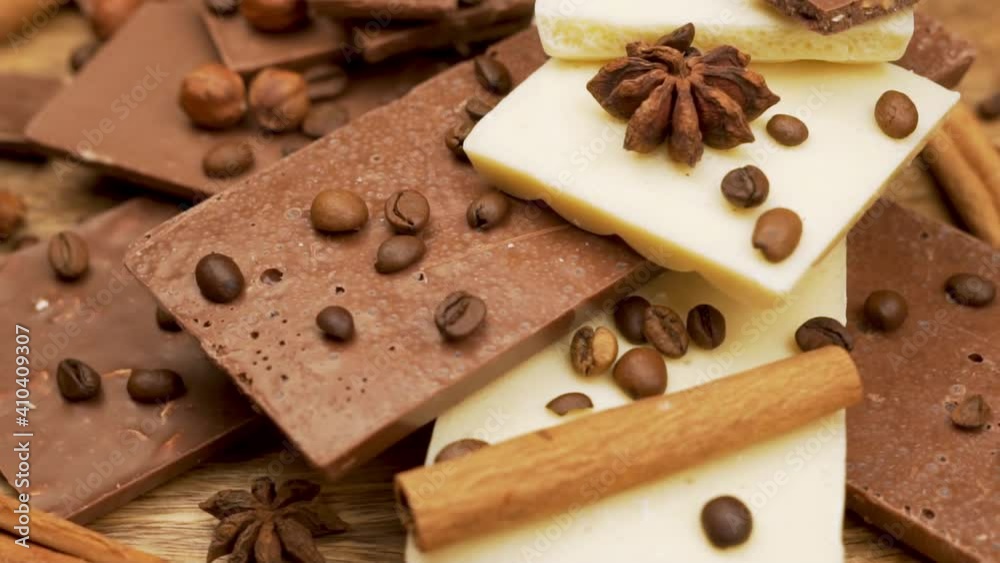 Broken Pieces and Tiles of Delicate Porous Milk and White Natural Chocolate Decorated with Hazelnuts Coffee Beans and Cinnamon Sticks, Close-up. Delicious Food. Sweets.