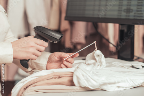 Woman cashier, seller scanning and reading barcode from clothes using barcode scanner in female clothing store.