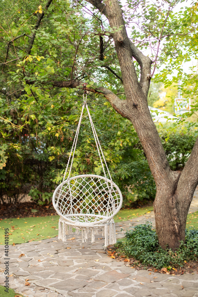 Comfortable hanging wicker white chair in summer garden. Cozy hygge place  for weekend relax in garden. Hammock chair in boho style hanging on tree.  Cozy exterior backyard. Concept of rest outdoor. foto