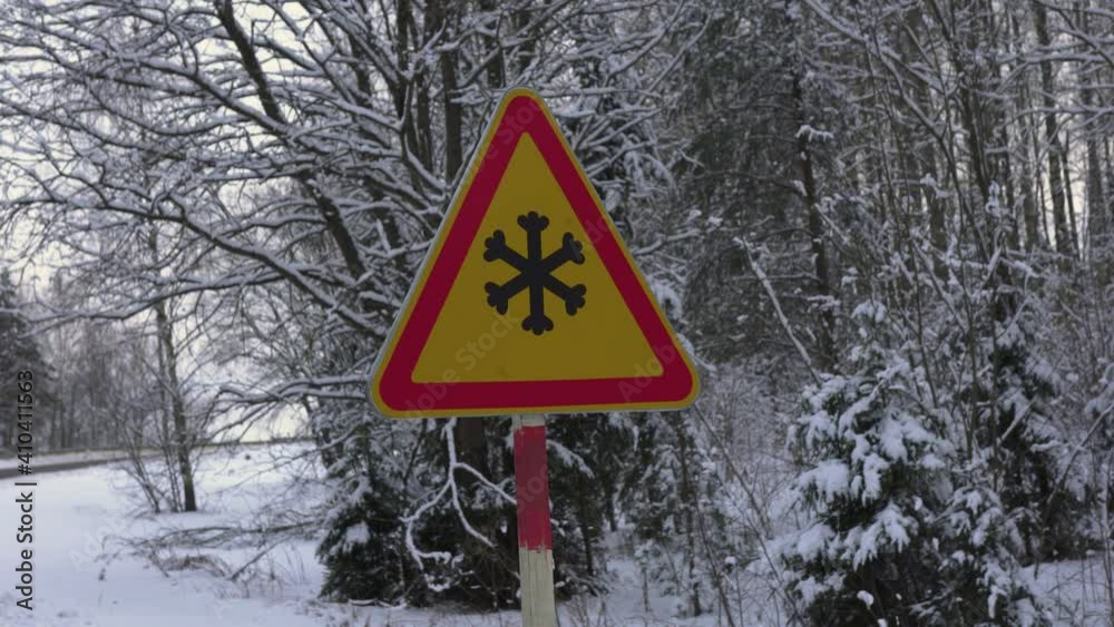 A road sign on a suburban forest road warns of snowy road surfaces and black ice. A road sign on a suburban forest road warns of snowy road surfaces and black ice.