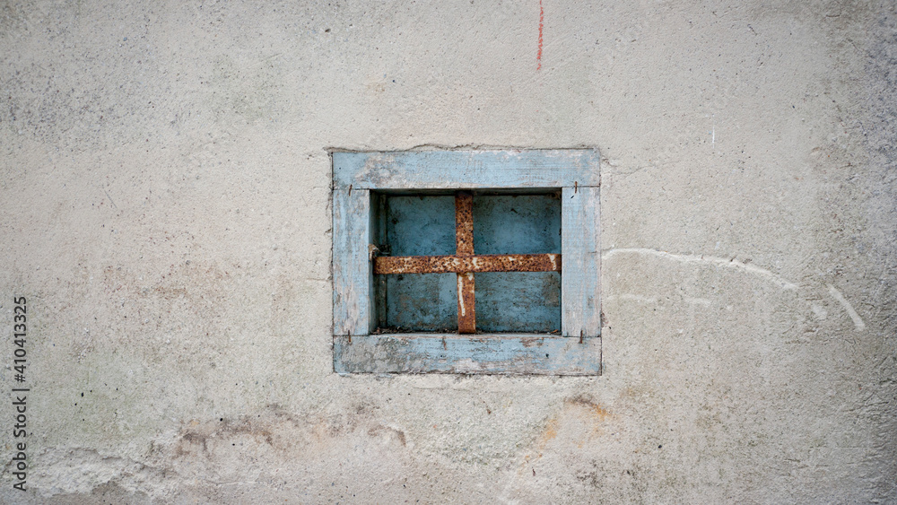 Pequeña ventana con reja oxidada en mro blanco con marco de madera azul  - obrazy, fototapety, plakaty 