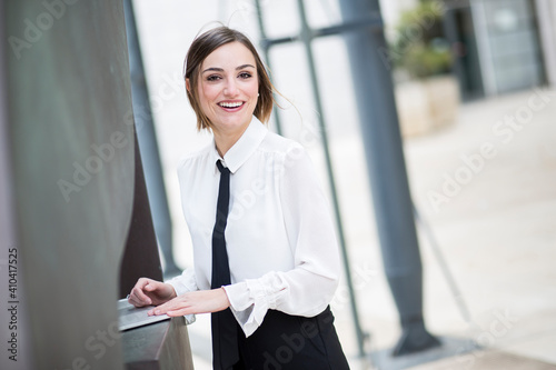 manager donna bionda con i capelli a caschetto, camicia bianca e cravatta nera, lavora al computer in esterni e sorride felice photo
