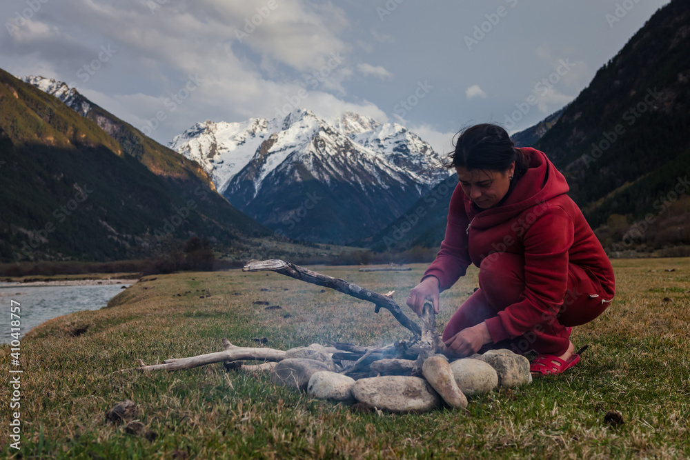 girl traveler in a camp at the foot of the mountain is makes a fire