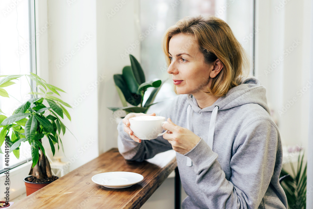 A woman is drinking coffee with pleasure in a light coffee shop by the window. A woman is drinking coffee with pleasure in a light coffee shop by the window.