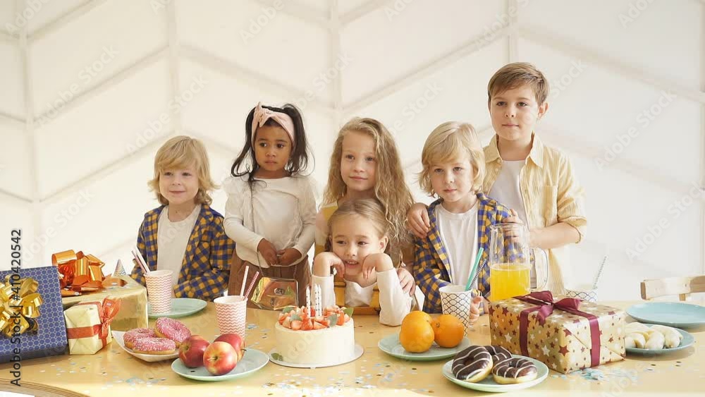 Children gathered at a festive table around the birthday girl, posing for a photographer taking memorable pictures. Children gathered at a festive table around the birthday girl, posing for a photographer taking memorable pictures.