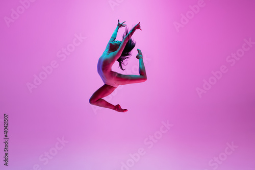 Fototapeta Naklejka Na Ścianę i Meble -  High above. Young and graceful ballet dancer on pink studio background in neon light. Art, motion, action, flexibility, inspiration concept. Flexible caucasian ballet dancer, moves in glow.