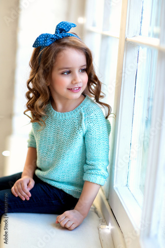 A cute girl with curls in a blue blouse and jeans is smiling. Fashion