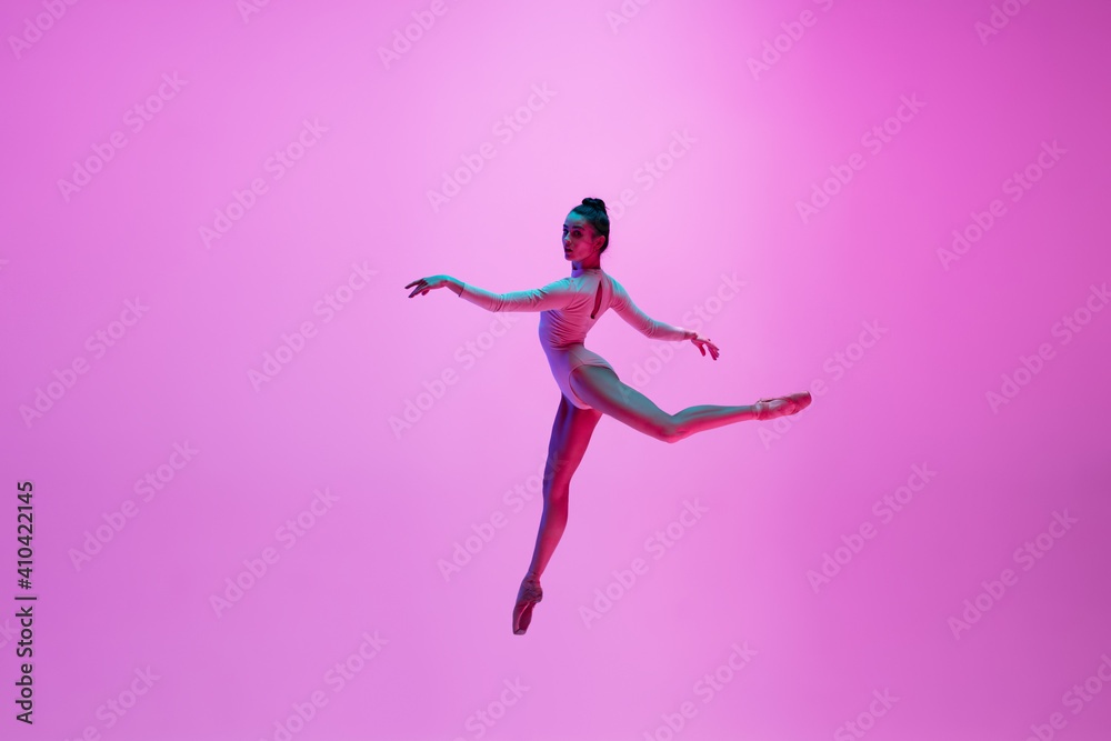 High above. Young and graceful ballet dancer on pink studio background in neon light. Art, motion, action, flexibility, inspiration concept. Flexible caucasian ballet dancer, moves in glow. High above. Young and graceful ballet dancer on pink studio background in neon light. Art, motion, action, flexibility, inspiration concept. Flexible caucasian ballet dancer, moves in glow.