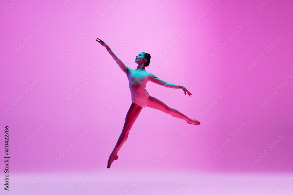 Flying, freedom. Young and graceful ballet dancer on pink studio background in neon light. Art, motion, action, flexibility, inspiration concept. Flexible caucasian ballet dancer, moves in glow.