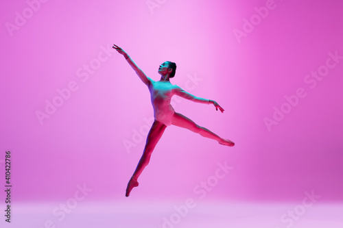 Flying, freedom. Young and graceful ballet dancer on pink studio background in neon light. Art, motion, action, flexibility, inspiration concept. Flexible caucasian ballet dancer, moves in glow.