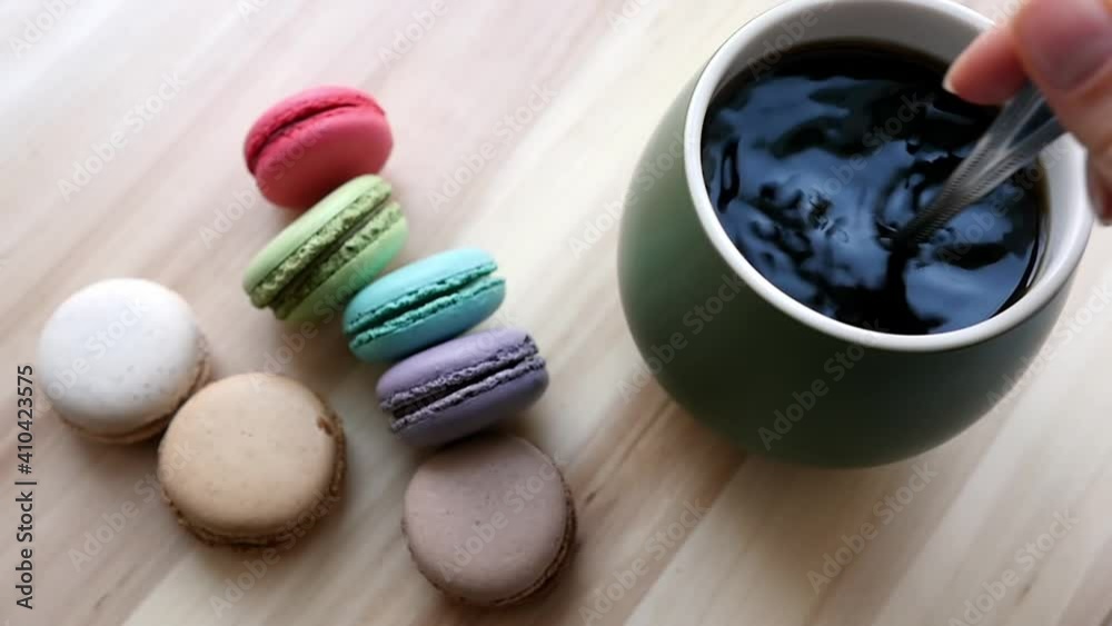 Strong black coffee and macaroons. Female hand stirring black coffee with a teaspoon Strong black coffee and macaroons. Female hand stirring black coffee with a teaspoon