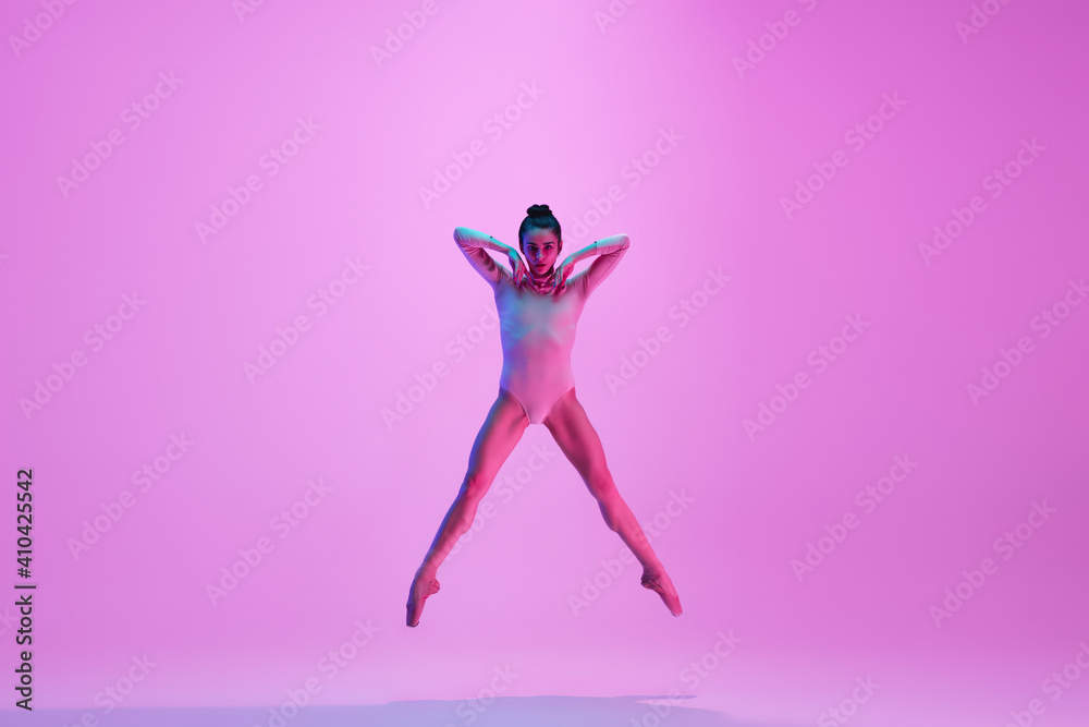 Flying on. Young and graceful ballet dancer on pink studio background in neon light. Art, motion, action, flexibility, inspiration concept. Flexible caucasian ballet dancer, moves in glow.