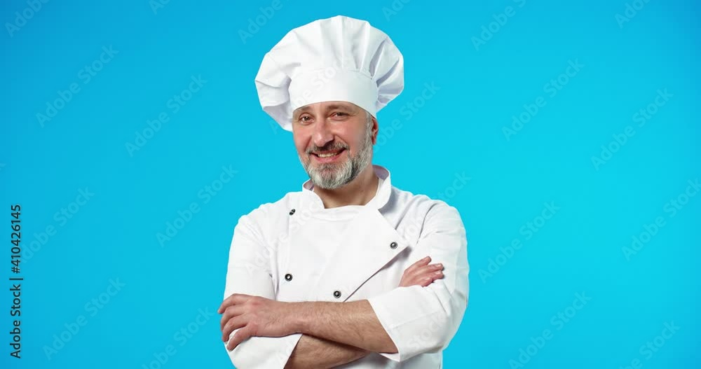 Close up portrait of Caucasian middle-aged happy smiling male cook in chef hat posing isolated on blue background in studio in positive mood, man baker looking at camera with smile on face Close up portrait of Caucasian middle-aged happy smiling male cook in chef hat posing isolated on blue background in studio in positive mood, man baker looking at camera with smile on face