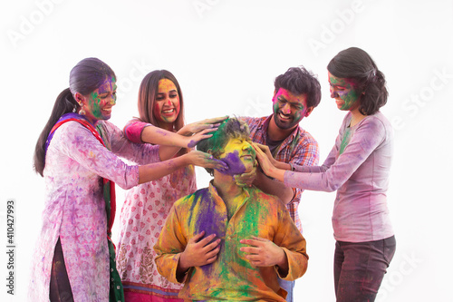 A HAPPY GROUP OF FRIENDS PUTTING GULAL ON ANOTHER FRIEND WHILE CELEBRATING HOLI 