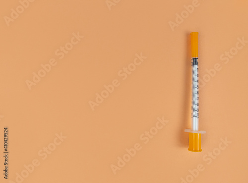 Insulin syringe on orange background with copy space.