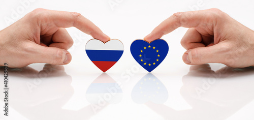 The concept of friendship and diplomatic relations between Russia and the European Union. Two male hands are holding flags in the shape of a heart on a glass table.  Two flags as a symbol of cooperati photo